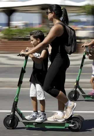Mãe e filho circulando pela cidade em patinetes elétricos